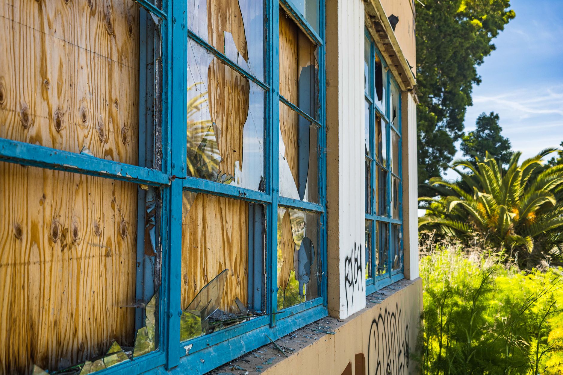 An abandoned building with broken windows and graffiti, surrounded by lush greenery in San Bernardino, CA