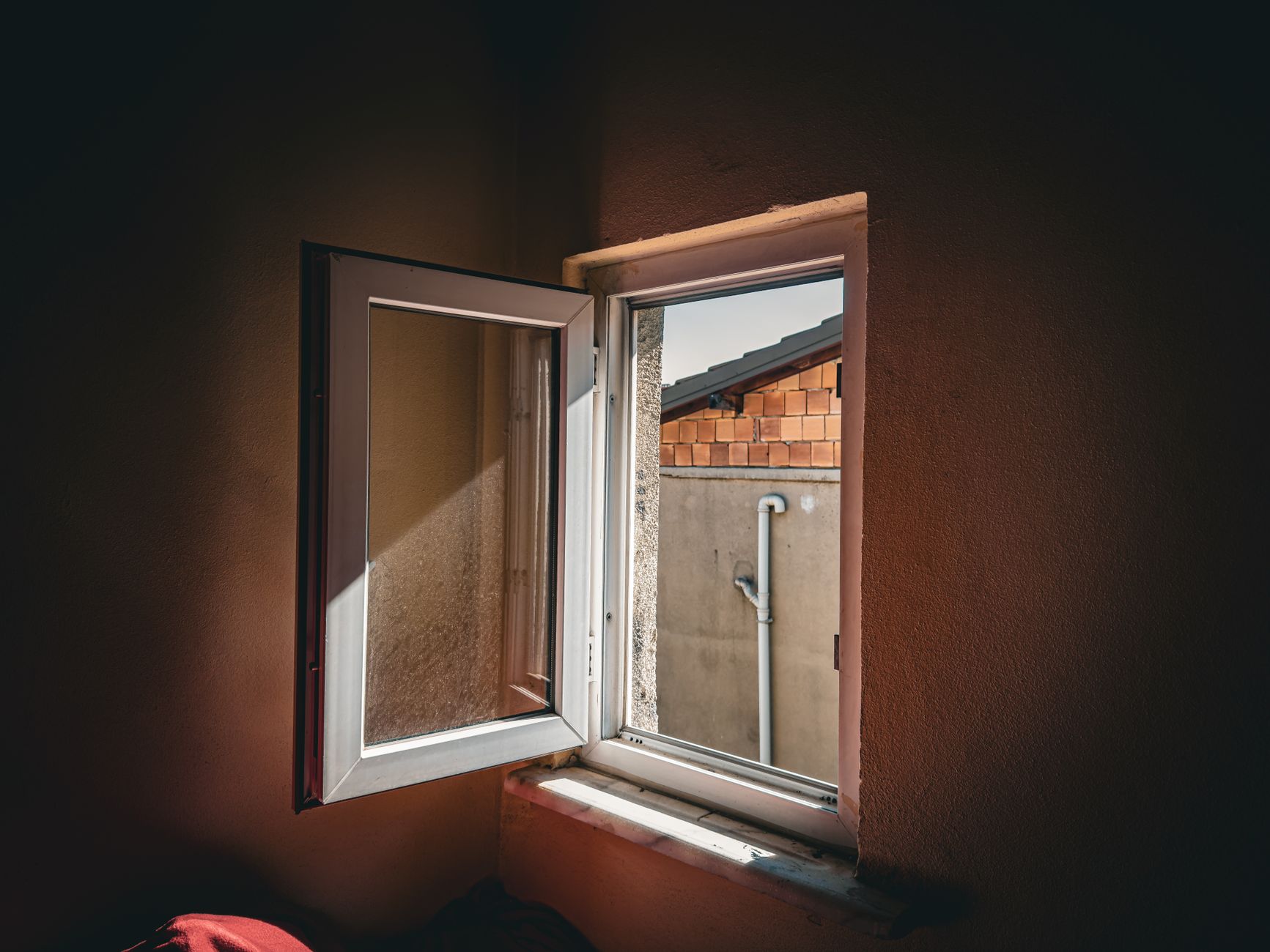 Open window view of a brick wall and pipe, sunlight casting shadows indoors in San Bernardino, CA